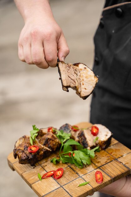 Fried ribs on a wooden plate on a gray surface. Barbecue decoration parsley and chili.