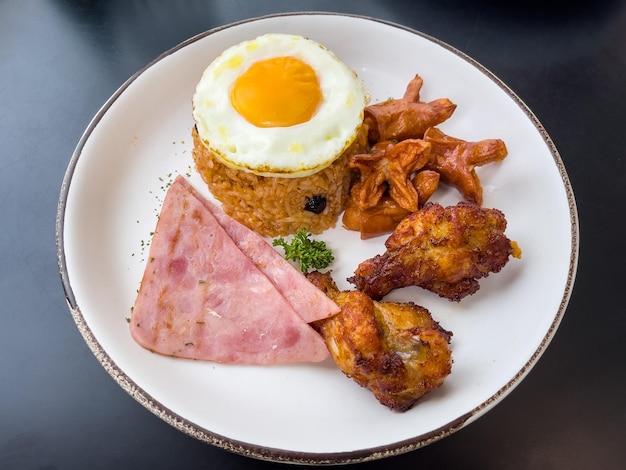 Foto riso fritto con uova fritte verdure hot dog prosciutto e ramoscelli di pollo fritto su un piatto sul tavolo