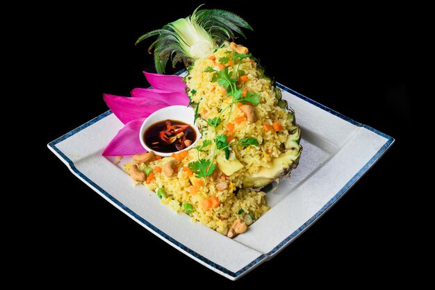 Fried rice with seafood in a pineapple with vegetables on blue plate isolated on black background si