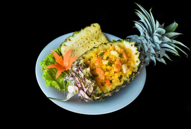 fried rice with seafood in a pineapple with vegetables on blue plate isolated on black background to