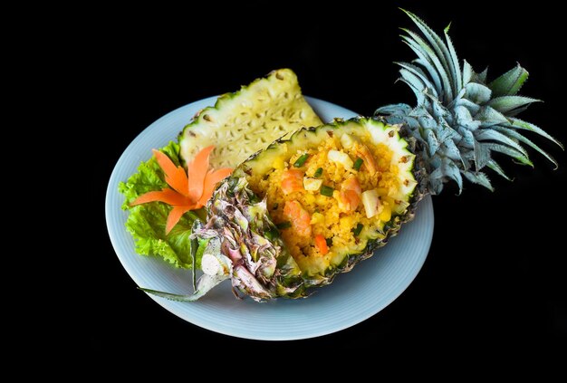 Fried rice with seafood in a pineapple with vegetables on blue plate isolated on black background to