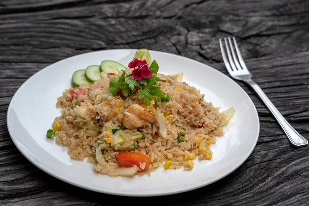 Fried rice with shrimps and vegetables in a white dish on an old wooden table, close up . Thai food , Thai cuisine. Fried rice with seafood in the restaurant