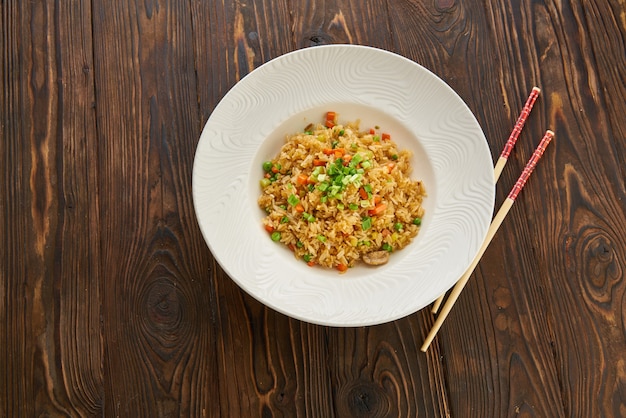 Fried rice with vegetables and beef in white plate, chopsticks on wooden table, Asian food concept, top view copy space