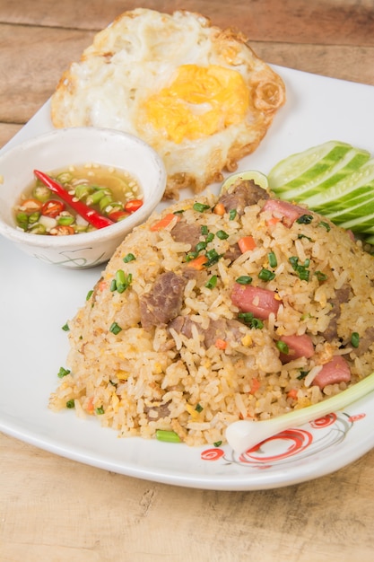 fried rice with vegetables, meat and fried eggs served on a plate with chopstick