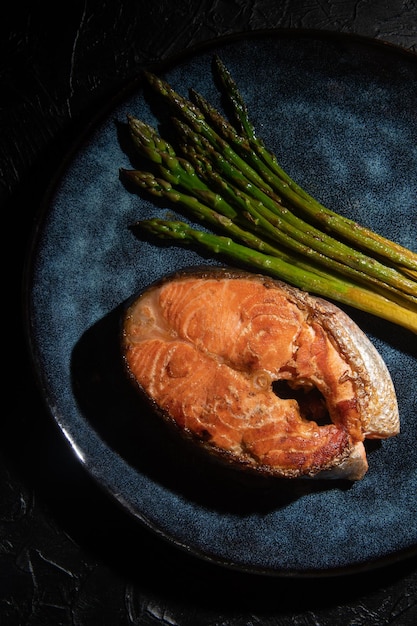 Fried salmon fillet with green asparagus on a dark background