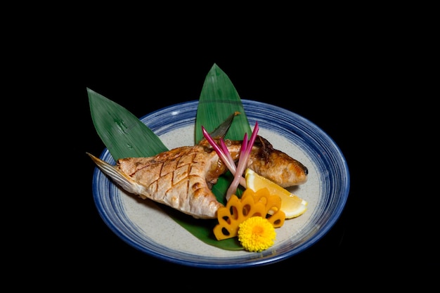 Photo fried salmon head comes with side dish and lemon on a white and blue plate on a black background