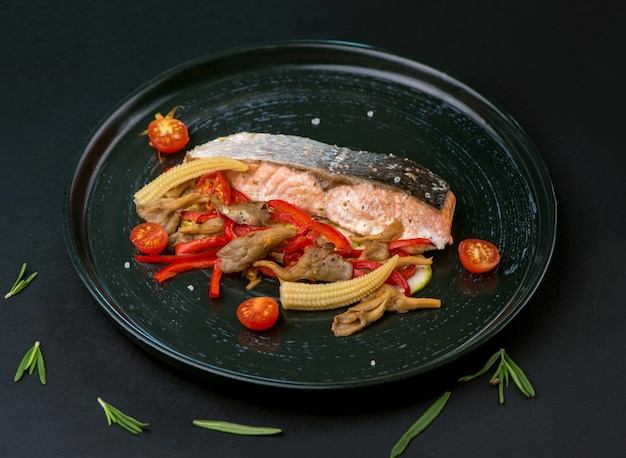 Жареный стейк из лосося с овощами на черном столе