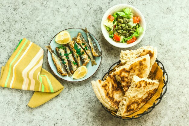 fried sardines on the plate decorated with lemon and parsley salad bowl and Arabic bread