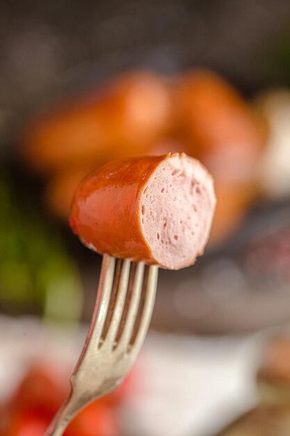 Fried sausage, with ketchup, on a fork, a frying pan on a wooden rustic table or background