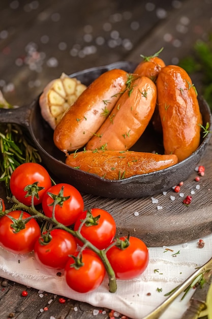 жареная колбаса, с кетчупом, на вилке, сковороде на деревянном деревенском столе или фоне