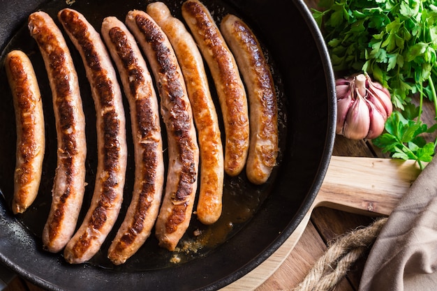 Fried sausages in iron cast pan, golden crust, garlic, parsley, kitchen table