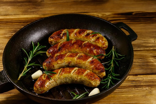 Fried sausages with rosemary garlic and spices in cast iron grill frying pan on wooden table