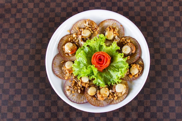 Fried scallops with garlic decorated with carrots on a white ceramic dish put on leather floor the grid pattern.