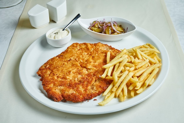 Fried schnitzel with french fries, sauces and salad on a white plate. Restaurant serving food. Flat lay