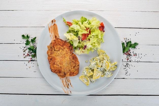 Photo fried schnitzel with potatoes and vegetables top view on a wooden background copy space