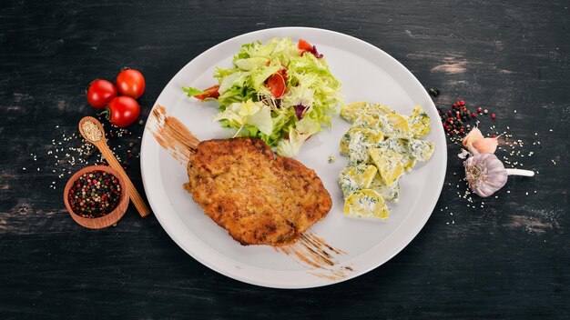 Fried schnitzel with potatoes and vegetables Top view On a wooden background Copy space