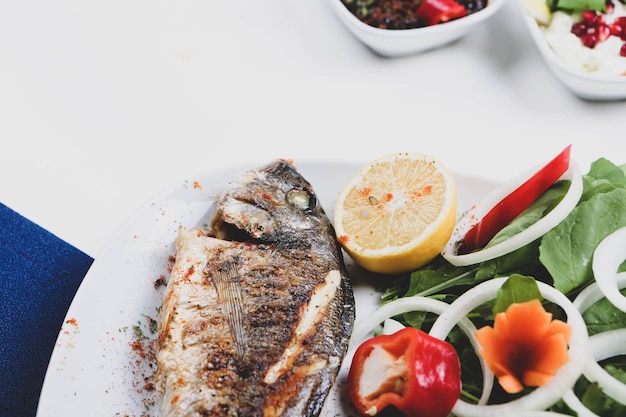 Fried sea bream cupra fish on white plate with onion garden rocket and lemon slices