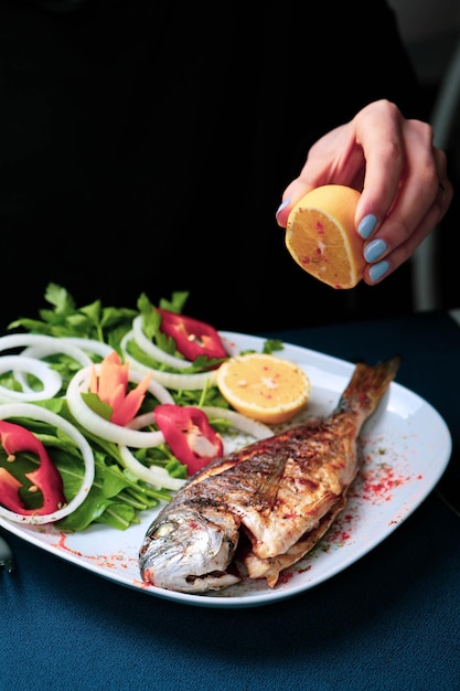 Fried sea bream cupra fish on white plate with onion garden rocket and lemon slices