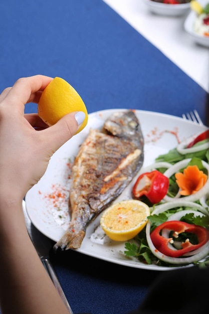 Fried sea bream (cupra) fish on white plate with onion, garden rocket and lemon slices