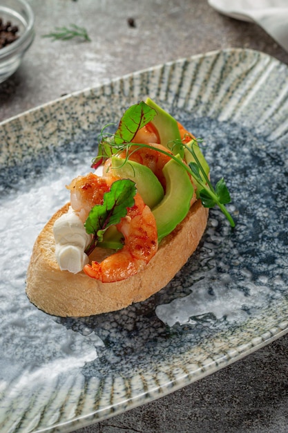 Fried shrimp and avocado sandwich on a plate of greens against a gray stone table