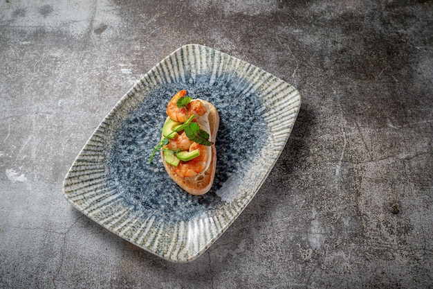 Gamberi fritti e sandwich di avocado su un piatto di verdure contro un tavolo di pietra grigia