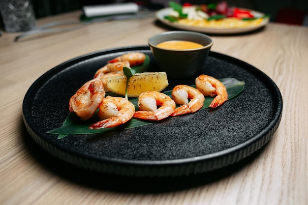 Fried shrimp on a green leaf with a slice of orange and yellow sauce on a black plate on a wooden table background
