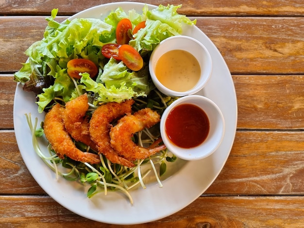 Fried shrimp salad with tartar sauce and tomato sauce on wooden background