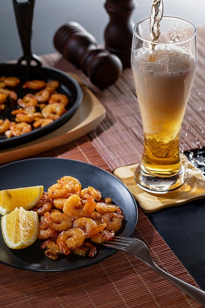 Gamberi fritti e limone in un piatto nero con un bicchiere di birra