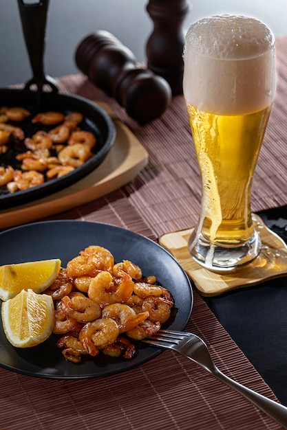 Gamberi fritti e limone in un piatto nero con un bicchiere di birra