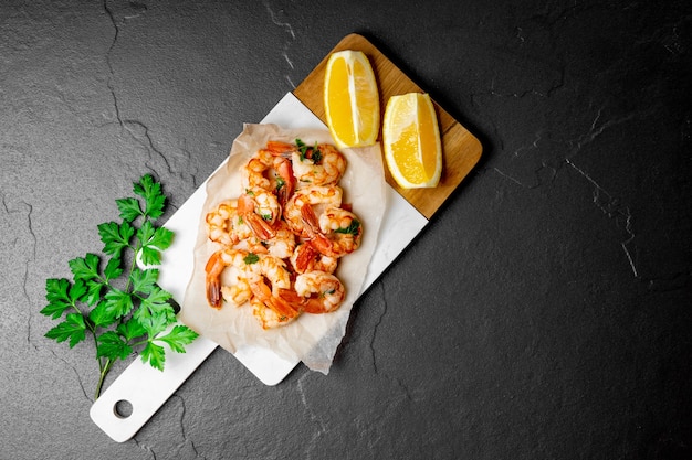 Fried shrimps with lemon on a cutting board and and black background, top view, free space for text