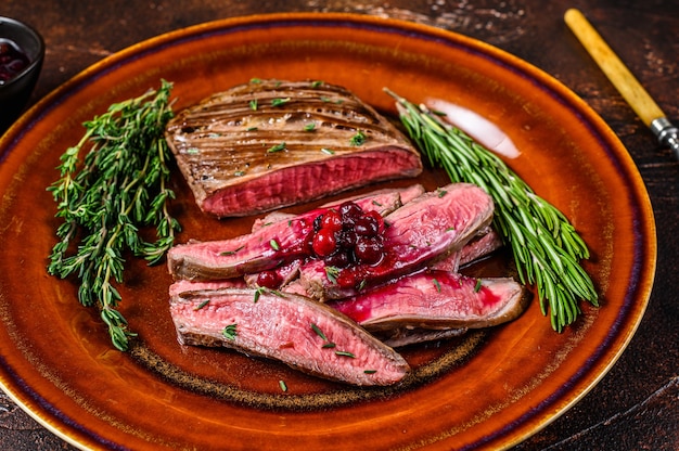 Fried sliced flank or bavette beef meat steak on a plate. Dark background. Top view.