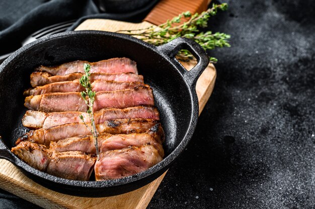 Bistecca di maiale di marmo affettata fritta in una pentola. carne biologica. sfondo nero.