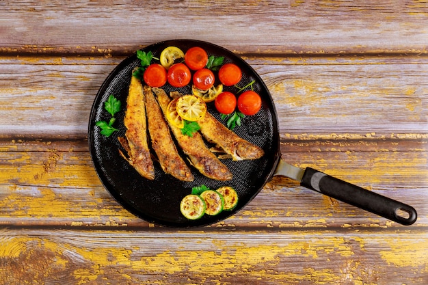 Piccolo pesce fritto in una pentola su un fondo di legno.