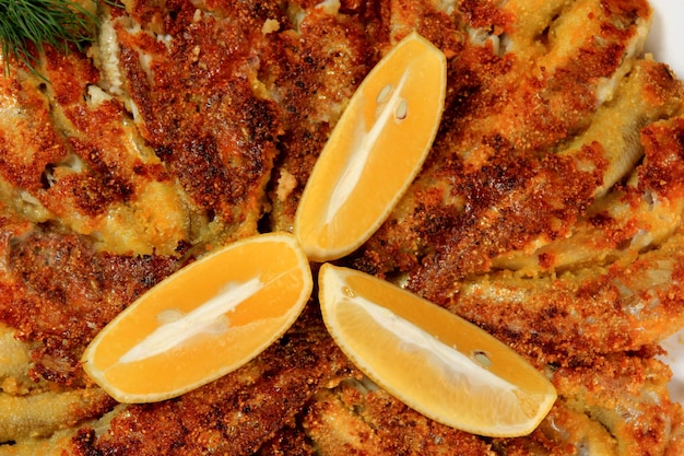 Fried small fish on a plate, decorated with lemon slices