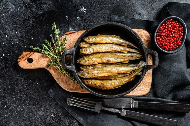 Fried smelt in the pan on the table with tomatoes and pepper