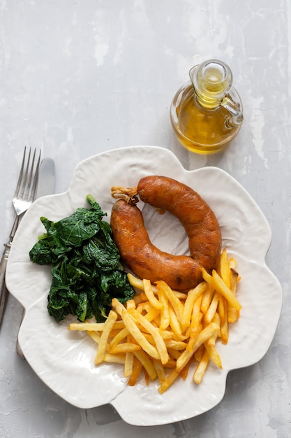 Fried smoked sausage with potato chips and greens on white plate