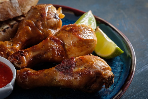 Fried spicy chicken legs in a ceramic dish with red sauce and lime