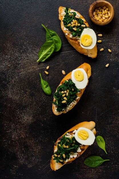 Fried spinach, egg and pine nuts sandwiches on brown vintage old concretesurface. Delicious healthy breakfast or snack. Top view.