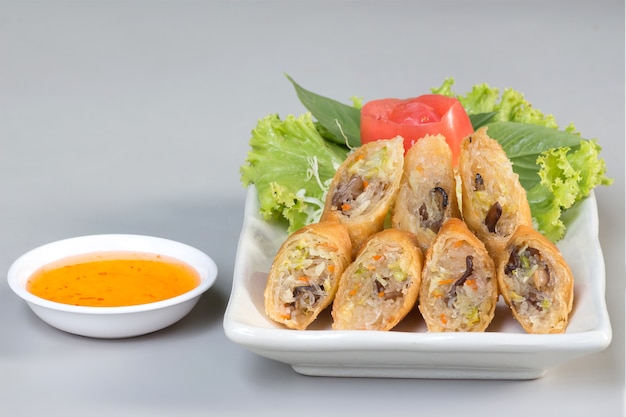 Fried spring rolls on white dish with sweet sauce on table