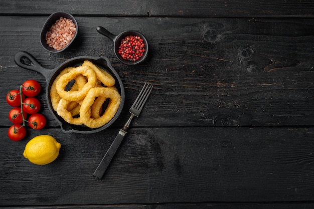 Anelli di calamari fritti antipasto di calamari impanati su padella in ghisa, su sfondo tavolo in legno nero, vista dall'alto piatta, con spazio copia per il testo