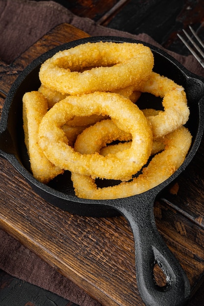 Fried squid rings breaded set on cast iron frying pan skillet, on old dark  wooden table background