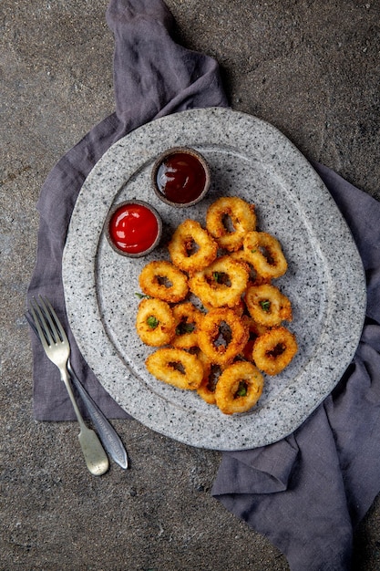 Fried squid rings on gray stone plate with sauces Gray concrete background