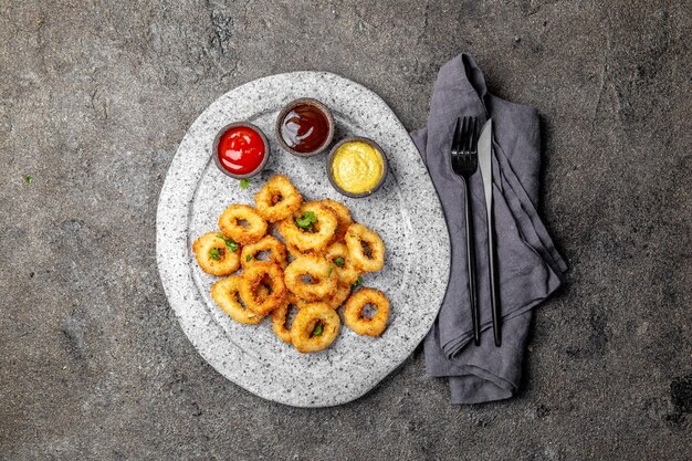 Foto anelli di calamari fritti su un piatto di pietra grigia con salse sullo sfondo di cemento grigio
