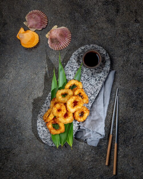 Fried squid rings on stone plate decorated with tropical leaves Asian food concept soy sauce and chopsticks