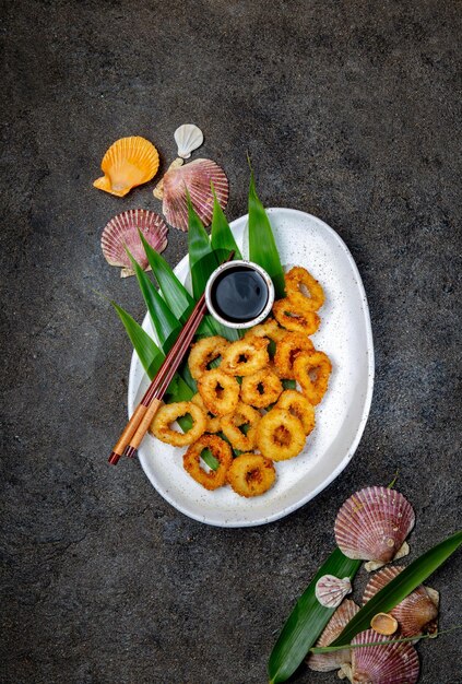 Photo fried squid rings on white plate decorated with tropical leaves gray concrete background top view