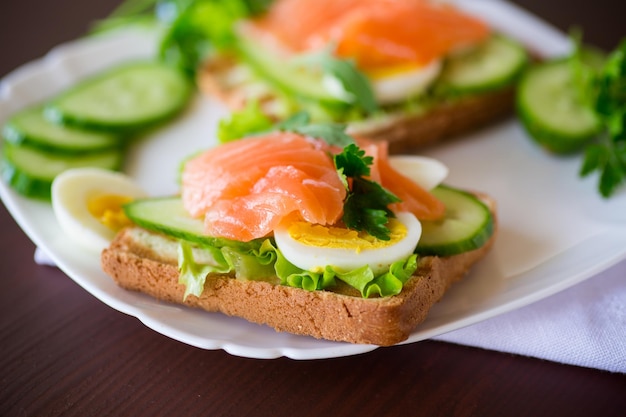 Photo fried toast with lettuce egg cucumbers and red fish in a plate on a wooden table