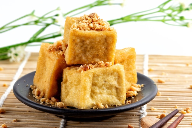 fried tofu is stacked sprinkled with peanuts on a black plate and chopsticks are placed on a wooden floor food of vegetarian popular food of vegetarian festival