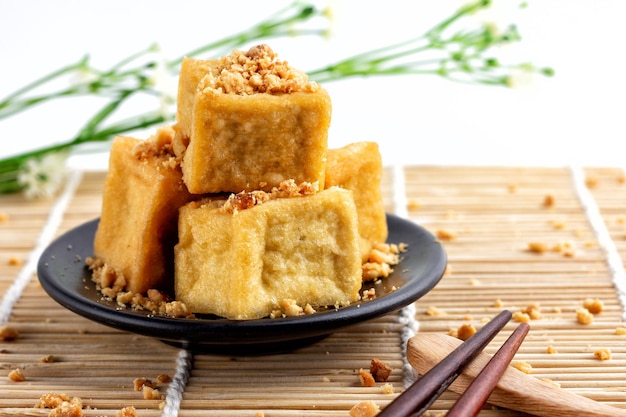 fried tofu is stacked sprinkled with peanuts on a black plate and chopsticks are placed on a wooden floor food of vegetarian popular food of vegetarian festival