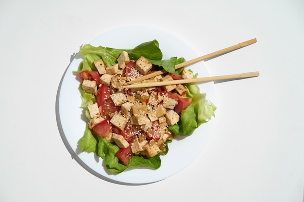 Fried tofu with vegetables and sesame seeds on white plate and whit background, view from top