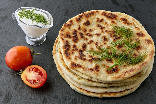 Fried tortillas with cheese and herbs, tomatoes and yogurt sauce on a dark stone table. Asian food